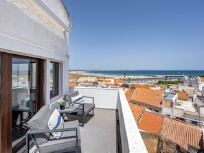 Ein Balkon mit Gartenmöbeln, freier Blick auf den Strand und die Küstenstadt.
