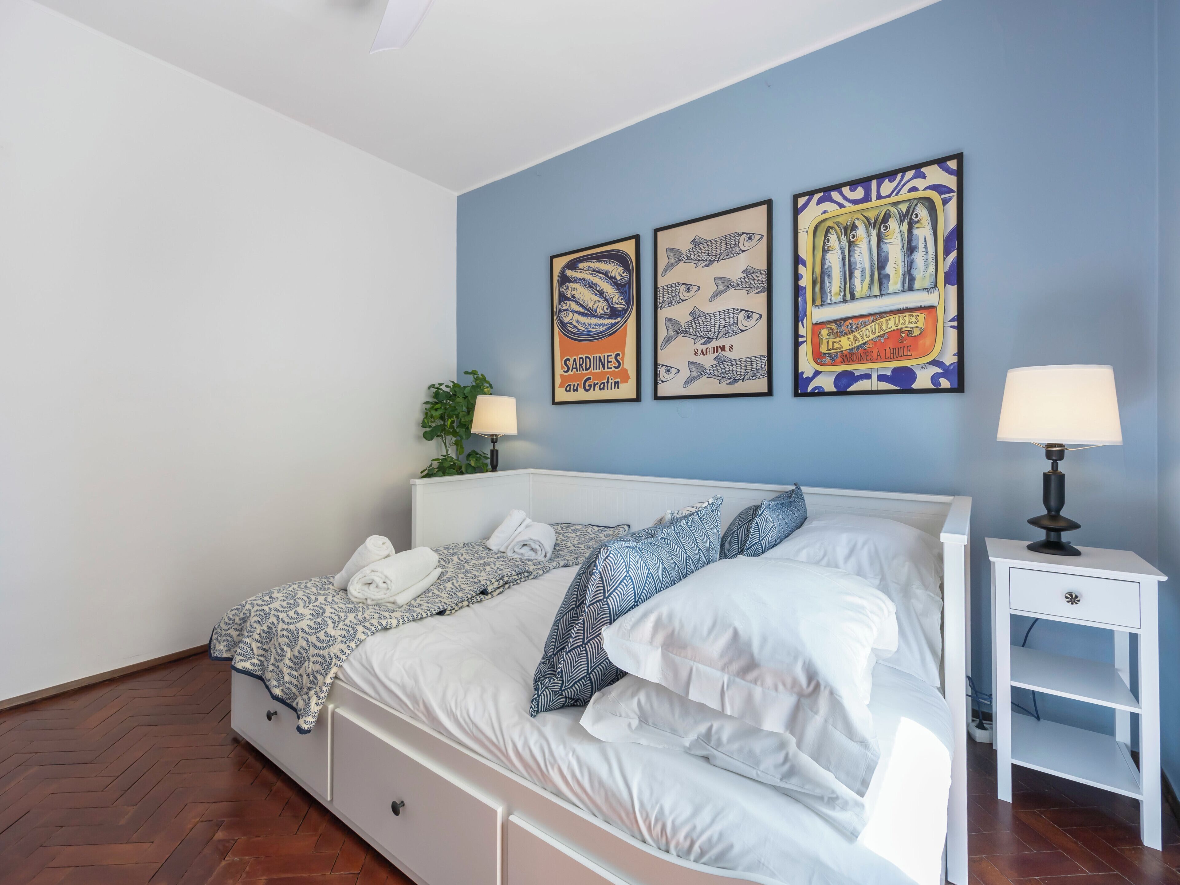 A double bed with white bedding, two bedside tables with lamps, and three framed posters on the wall.