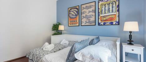 A double bed with white bedding, two bedside tables with lamps, and three framed posters on the wall.