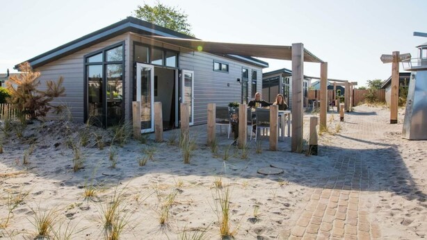 A modern beach house with a glass door entrance, a covered patio, and a brick pathway. - Duinlodge 4 + 2 (Noordwijk)
