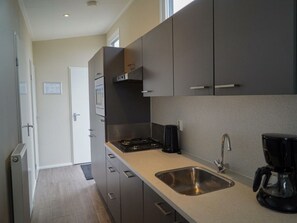 A modern kitchen with grey cabinets, a stainless steel sink, and a coffee maker. - Duinlodge 4 + 2 (Noordwijk)