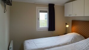 A bedroom with two beds, a window with a curtain, a bedside lamp, and a radiator. - Duinlodge 4 + 2 (Noordwijk)