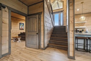 Ein Holzinnenraum mit einer Treppe zu einem Erkerbereich, einer Küche mit Barhocker und einem gerahmten Bild an der Wand.