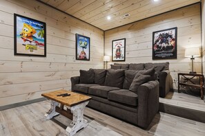 Ein Zimmer mit einem grauen Sofa, einem Holztisch und Postern an den Wänden.