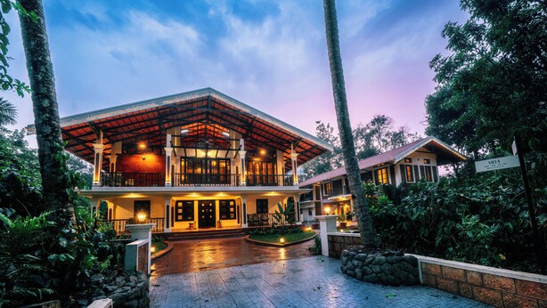 A two-story building with a covered entrance, a stone wall, and a paved driveway. - Kumberi Manor by Raho Heritage Retreat in Coorg (Ammathi)