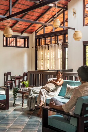 A room with a high ceiling, wooden beams, a sofa, a table with chairs, and hanging lamps. - Kumberi Manor by Raho Heritage Retreat in Coorg (Ammathi)