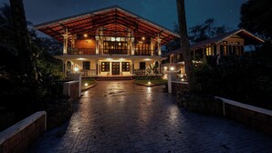 A large, two-story house with a covered porch, a stone pathway leading to the entrance, and a starry night sky. - Kumberi Manor by Raho Heritage Retreat in Coorg (Ammathi)