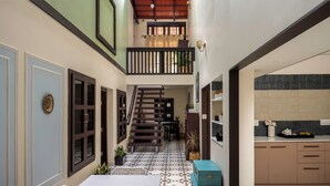 A dining area with a table set for two, a staircase leading to an upper level, and a kitchen area with cabinets and a countertop. - Kumberi Manor by Raho Heritage Retreat in Coorg (Ammathi)