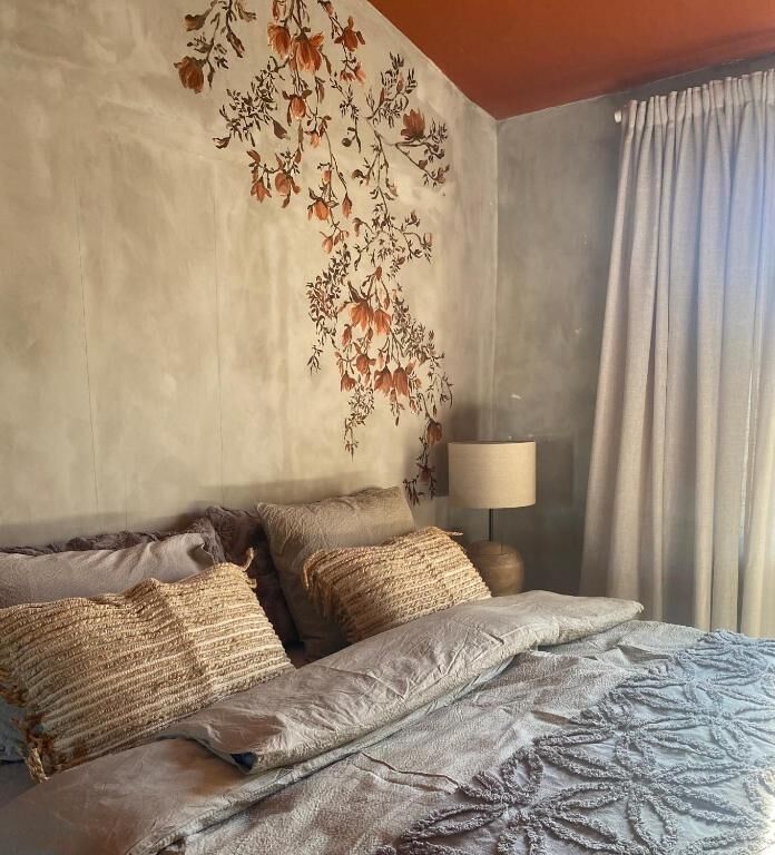 Un dormitorio con cama, almohadas, una lámpara y una pared con estampado floral.
