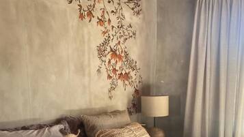 Un dormitorio con cama, almohadas, una lámpara y una pared con estampado floral.