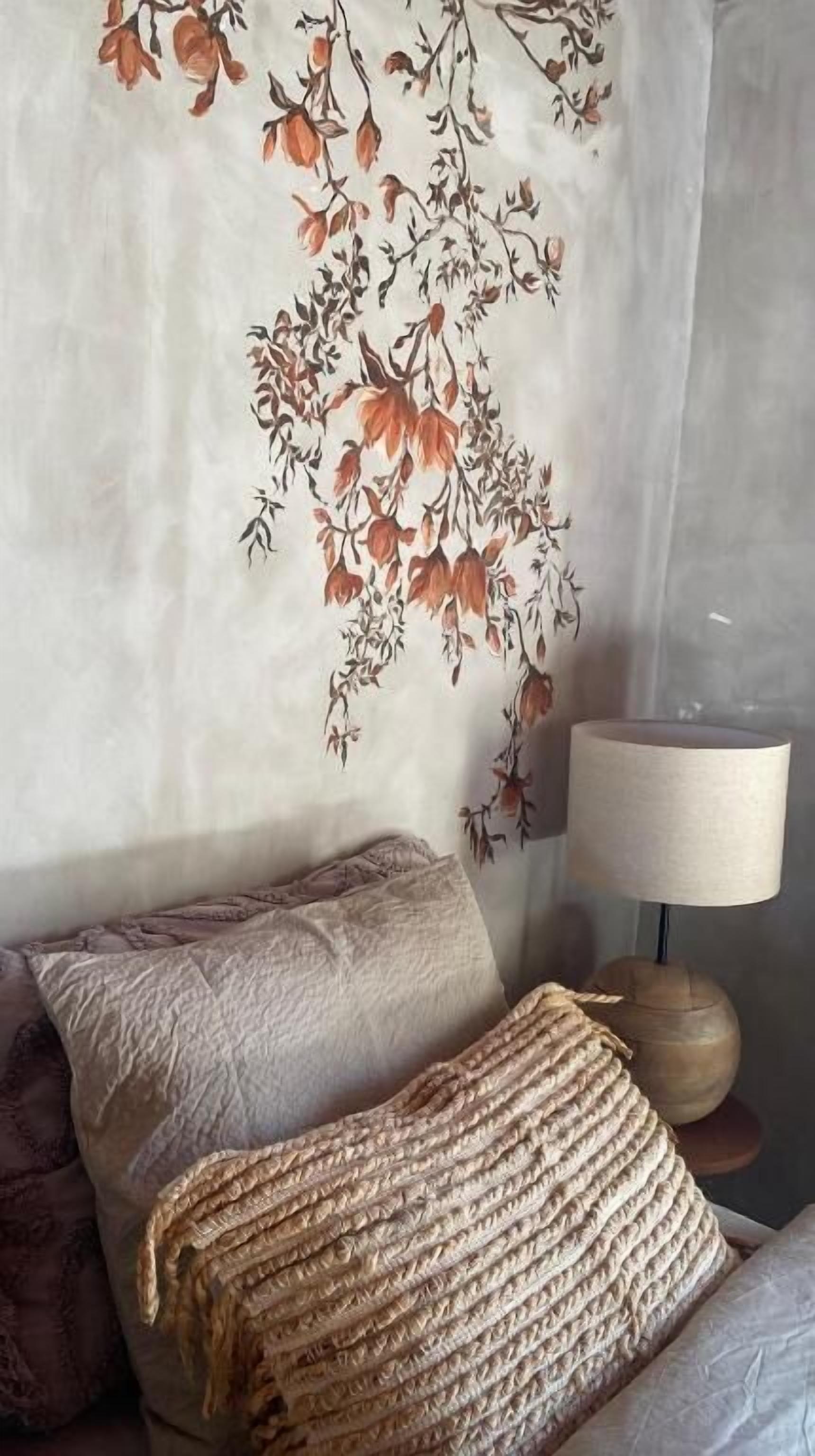 A bedroom with a bed, pillows, a lamp, and a wall with a floral design.