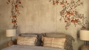 Un dormitorio con cabecera curva, cama con cubrecama estampado, dos lámparas de noche y una pared decorativa con diseños florales.