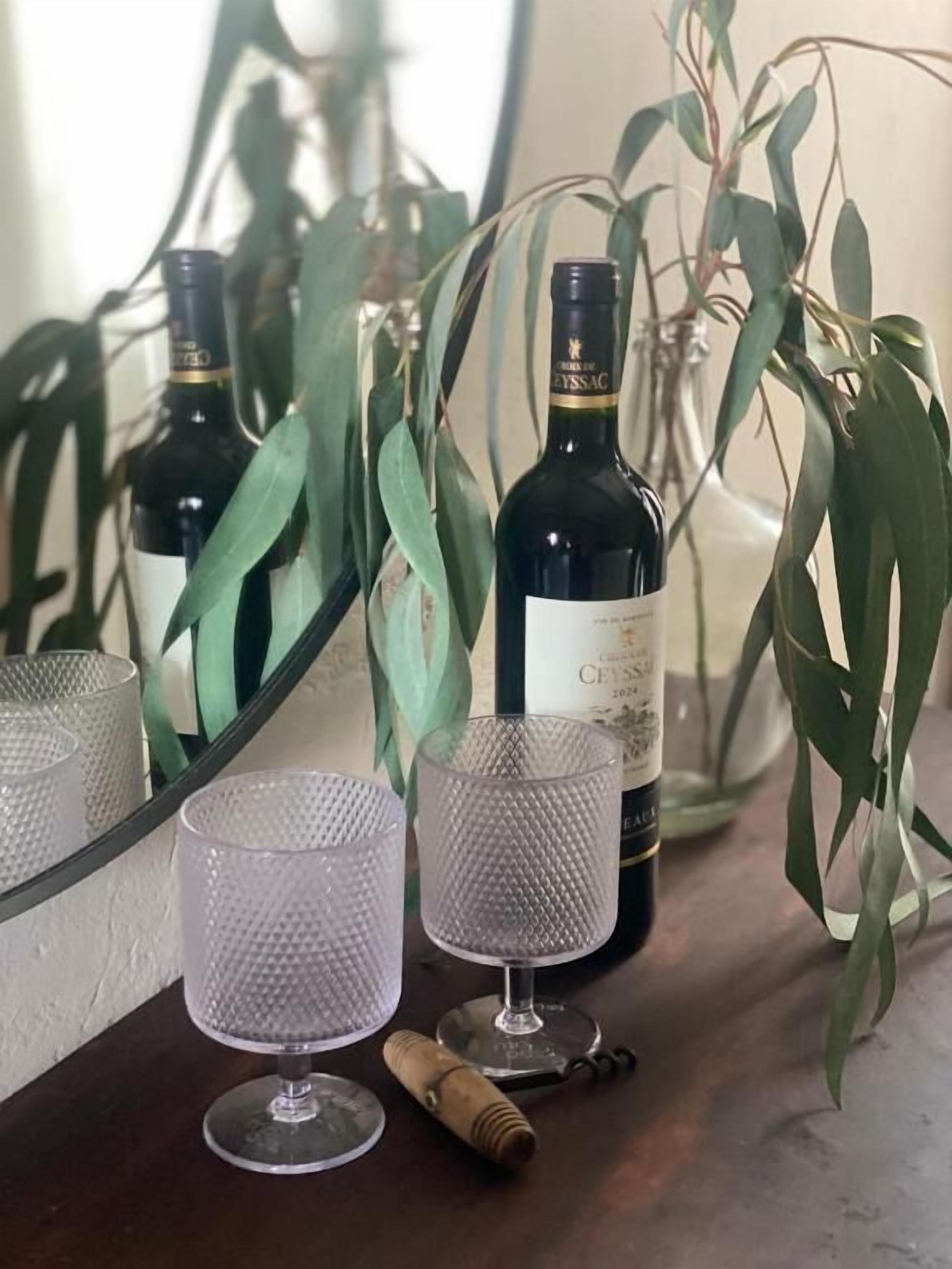 A bottle of wine, two glasses, and a cork on a table with a mirror and green plants.