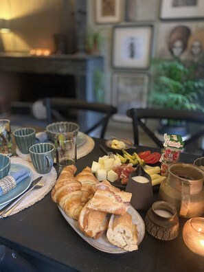 A breakfast table with croissants, cheese, fruits, and a coffee pot.