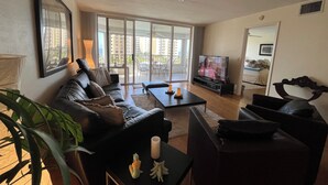A living room with a sofa, coffee table, TV, and a balcony with a view of buildings. - Apartment in Paradise! Feb/March 2027 availability! (Naples)