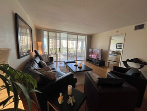 Ein Wohnzimmer mit einer Couch, einem Couchtisch, einem Fernseher und einem Balkon mit Blick auf Gebäude.