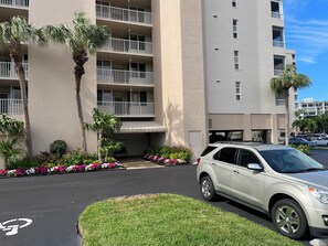 Un immeuble à plusieurs étages doté de balcons, d’un espace de stationnement et d’un VUS blanc garé devant.