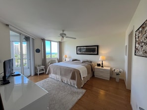 Ein Schlafzimmer mit Bett, Nachttischen, Deckenventilator, Fernseher und Blick ins Freie.