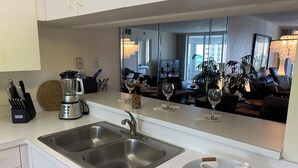 A modern kitchen with a double sink, a coffee maker, and a blender. There is a dining area with a table and chairs visible through a large mirror. - Apartment in Paradise! Feb/March 2027 availability! (Naples)