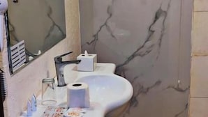 A bathroom with a marble wall, a sink with toiletries, a mirror, and a fan. - Al Orouba Hotel (Riyadh)