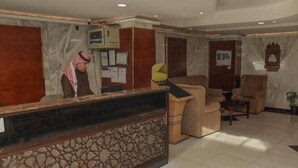 A hotel reception area with a marble reception desk, a man standing behind it, and several beige armchairs. - Al Orouba Hotel (Riyadh)