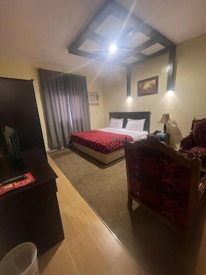 A hotel room with a bed, a desk, a chair, a lamp, and a ceiling light. - Al Orouba Hotel (Riyadh)