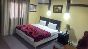 A hotel room with a bed, curtains, a nightstand, a lamp, a chair, and a picture on the wall. - Al Orouba Hotel (Riyadh)