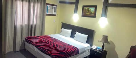 A hotel room with a bed, curtains, a nightstand, a lamp, a chair, and a picture on the wall.