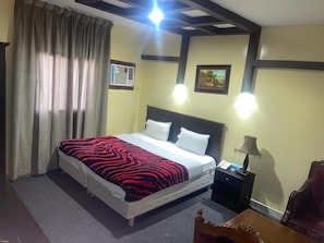A hotel room with a bed, curtains, a nightstand, a lamp, a chair, and a picture on the wall. - Al Orouba Hotel (Riyadh)