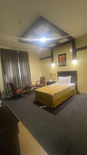Ein Hotelzimmer mit Bett, Schreibtisch, Stuhl, Nachttisch und einem Fenster mit Vorhängen.