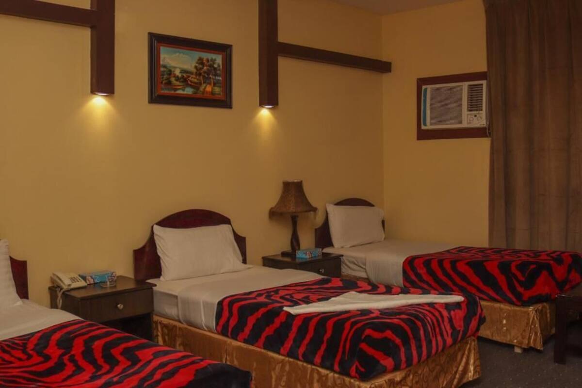 A hotel room with two beds, a nightstand, a lamp, a painting on the wall, and an air conditioning unit.