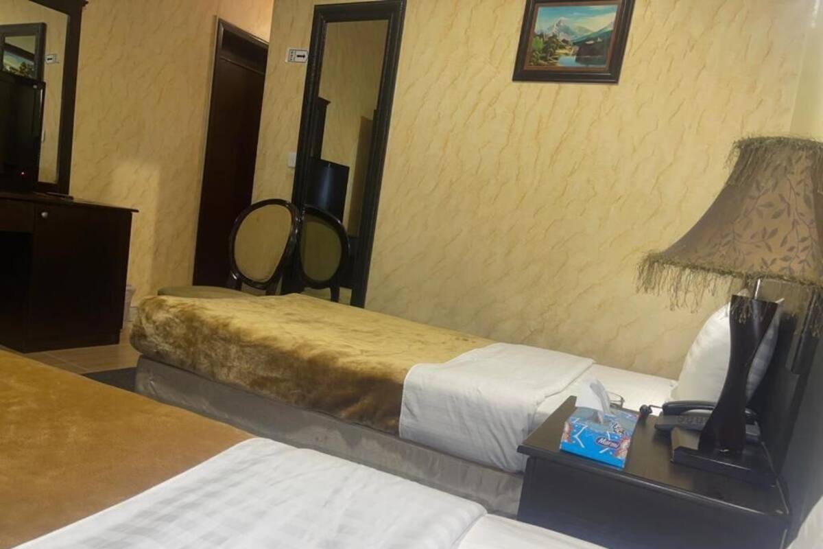 A hotel room with a bed, a desk with a lamp, a chair, a mirror, and a picture on the wall.