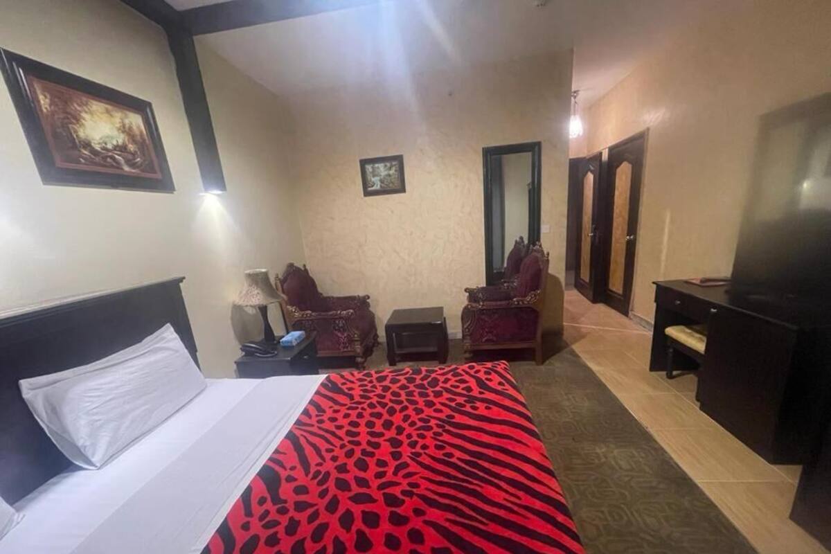 A hotel room with a bed, a desk, a chair, a TV, and a mirror.