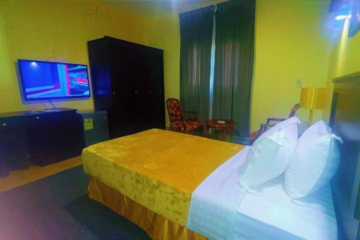 A hotel room with a bed, a television, a wardrobe, a chair, and a small table.