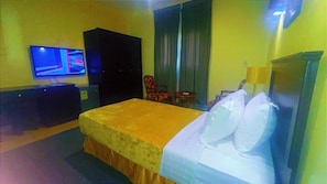 Ein Hotelzimmer mit Bett, Fernseher, Kleiderschrank, Stuhl und kleinem Tisch.
