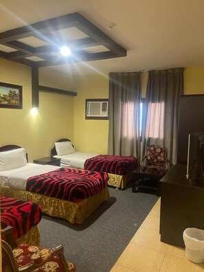 A hotel room with two beds, a desk, a chair, an air conditioning unit, and a television. - Al Orouba Hotel (Riyadh)