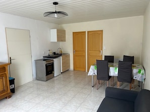 A compact kitchen with a stove, sink, and cabinets, a dining area with a table and chairs, and a ceiling fan.
