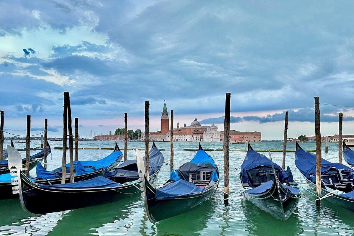 Gondolas docked at a Venetian marina with a historic building in the background.