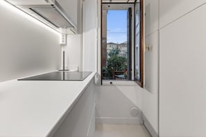 Eine schmale Küche mit Fenster, weißen Wänden und Blick auf Gebäude.