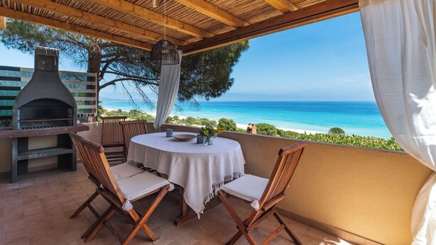 Eine Terrasse im Freien mit einem runden Tisch, zwei Stühlen, einem Grill und Blick auf den Ozean.