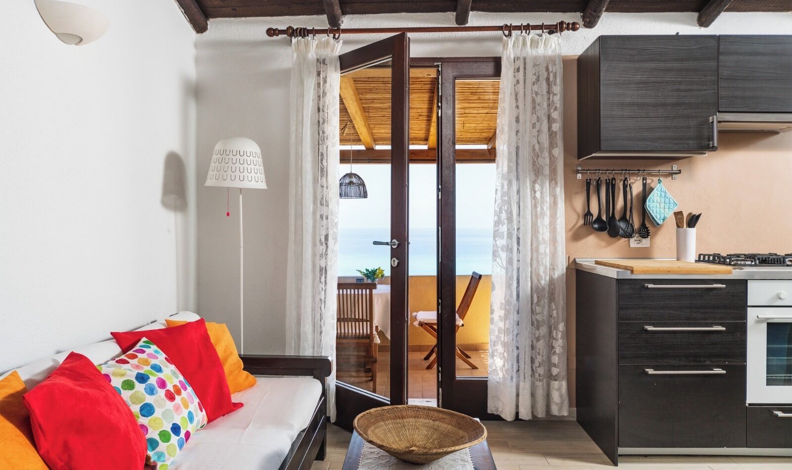 Un salon avec un canapé, un coin repas avec une table, une cuisine équipée de placards et d’une cuisinière, et un balcon avec vue.