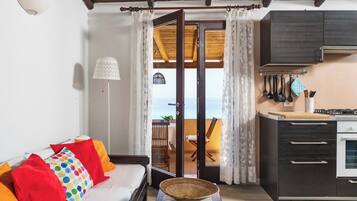 Un salon avec un canapé, un coin repas avec une table, une cuisine équipée de placards et d’une cuisinière, et un balcon avec vue.