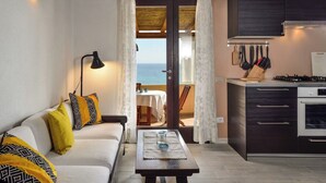 Ein gemütliches Zimmer mit einer Couch, einem Tisch, einer Küche mit Herd und Blick aufs Meer.