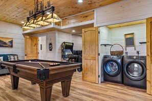 A pool table in a room with wooden floors and walls, a washing machine, and a door leading to another room. - Nice Views, Theater, Gameroom, Arcade, Hot Tub (Pigeon Forge)
