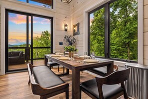 Un comedor con una mesa de madera dispuesta para cuatro, ventanas amplias y vistas a la vegetación.