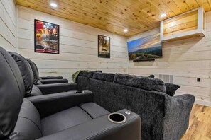 A room with a wooden ceiling, a black leather sofa, and two framed posters on the wall. - Nice Views, Theater, Gameroom, Arcade, Hot Tub (Pigeon Forge)