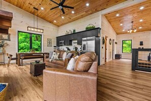 A spacious living room with a leather sofa, wooden flooring, and a ceiling fan. - Nice Views, Theater, Gameroom, Arcade, Hot Tub (Pigeon Forge)