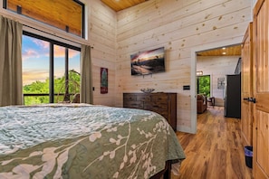 A bedroom with a large bed, a TV, a fireplace, and a view of the outdoors. - Mountain View Lodge, Hot Tub, Fire Table & Theater (Pigeon Forge)