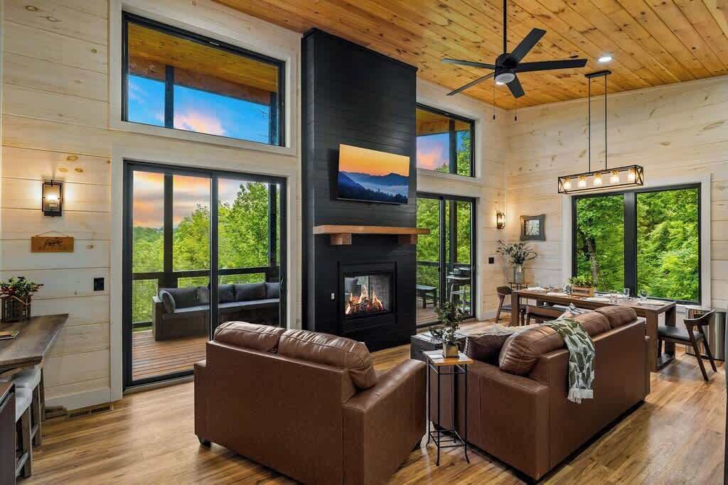 A modern interior with a fireplace, leather sofas, and large windows offering a view of greenery.