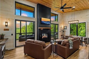 Un interior moderno con chimenea, sofás de cuero, suelos de madera y ventanas amplias que ofrecen vistas al exterior.